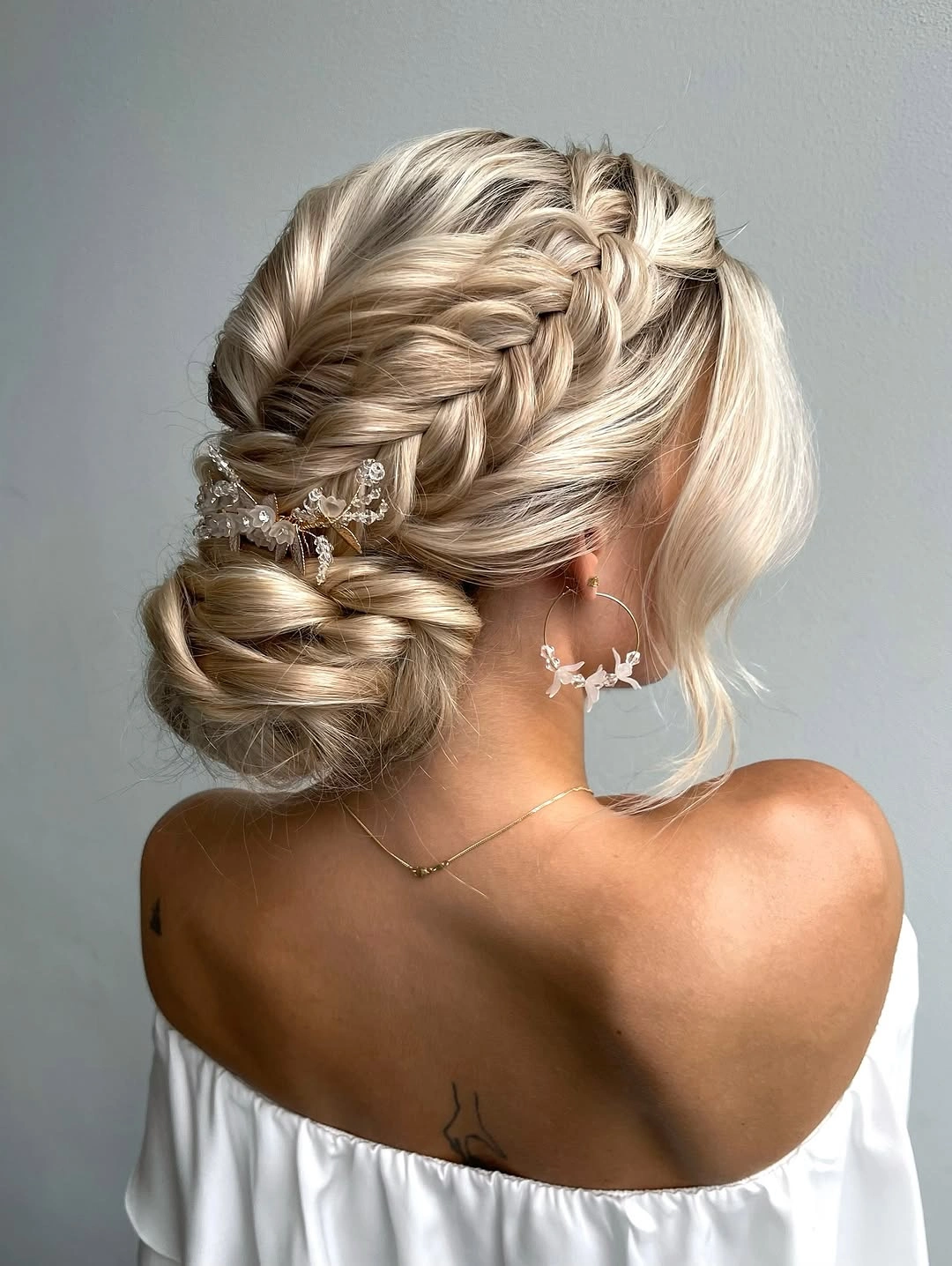 Fall hairstyles for wedding guests 2026 Romantic Braided Low Bun with Soft Blonde Dimension