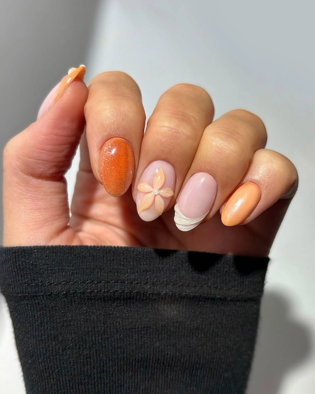 orange shimmer almond nails with flower accent and wavy French edge