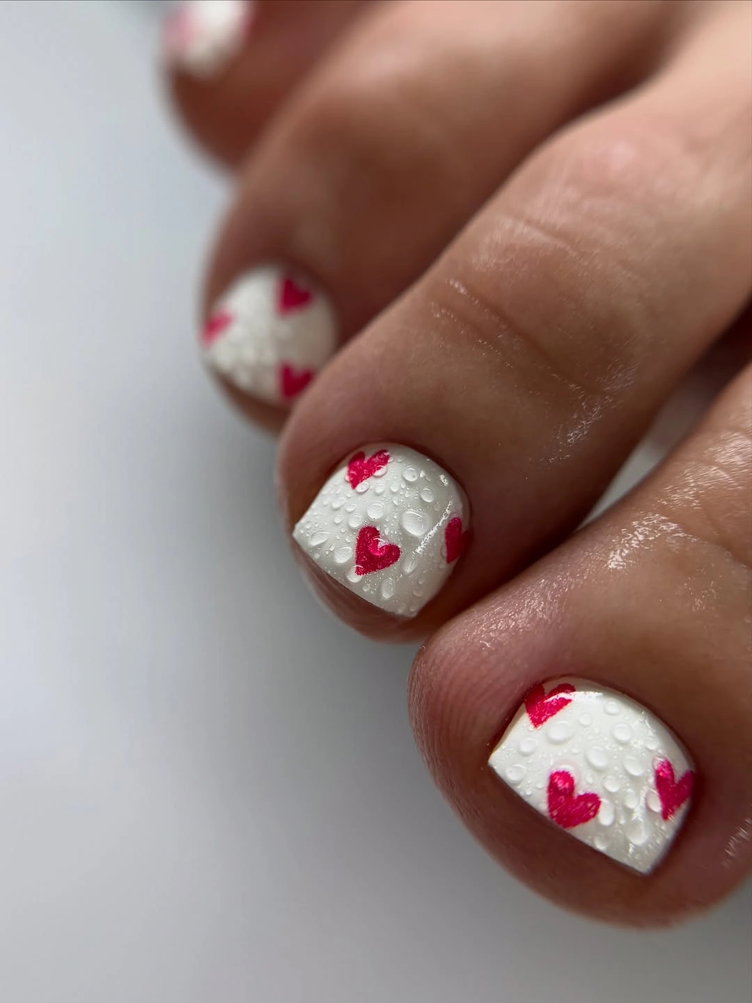 white pedicure with pink hearts and dewy texture