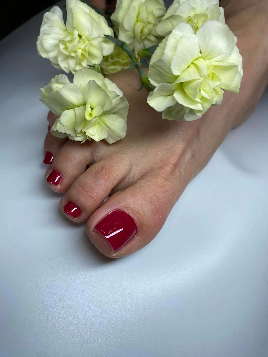 glossy red pedicure styled beside cream flowers