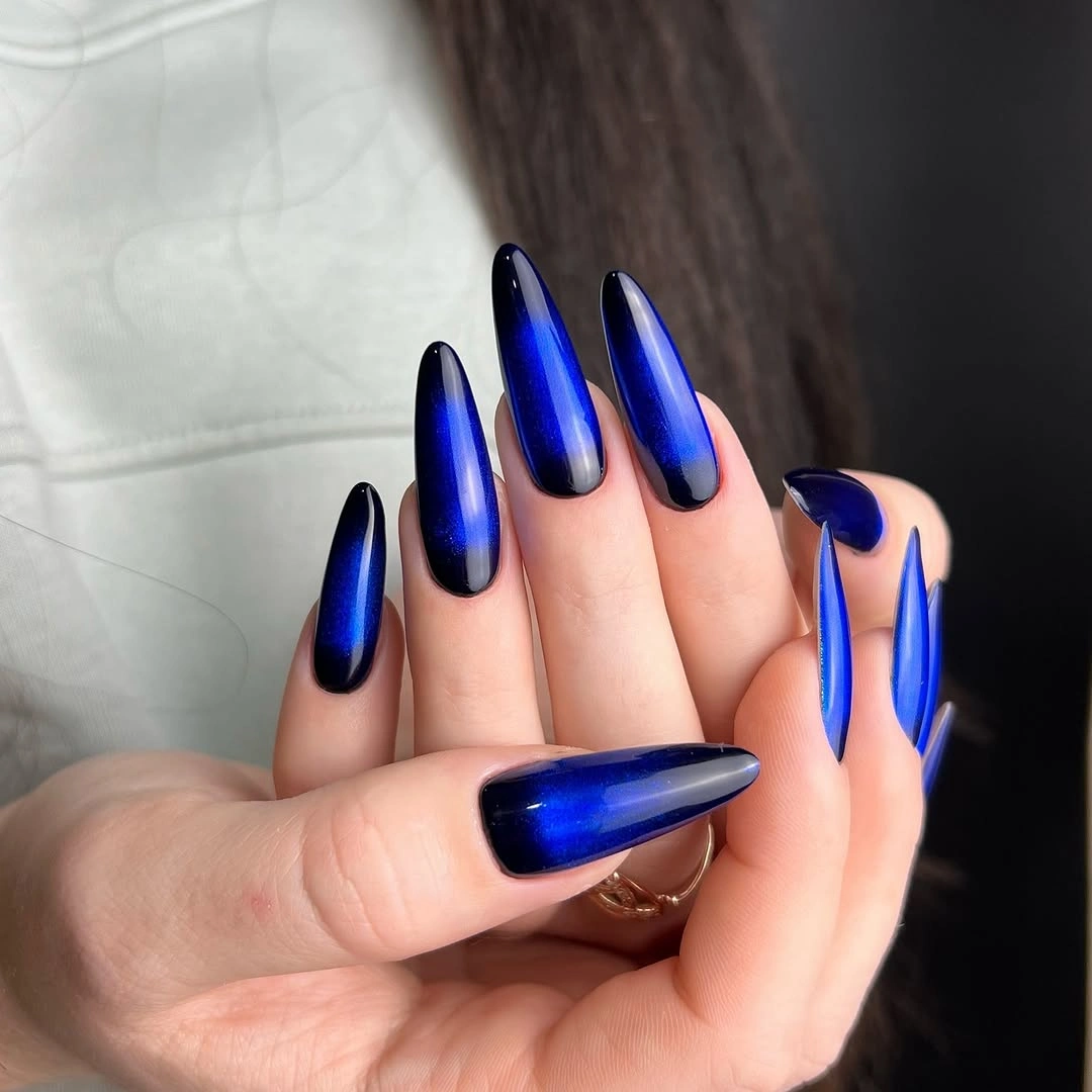 Long glossy cobalt-blue pointed nails against white clothing