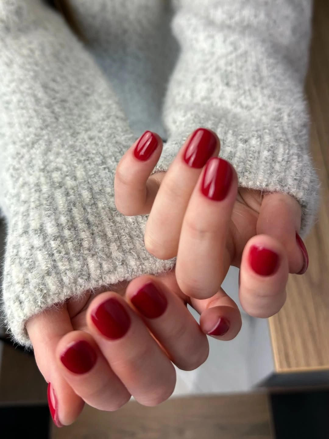 Short glossy red rounded-square nails framed by gray knitwear