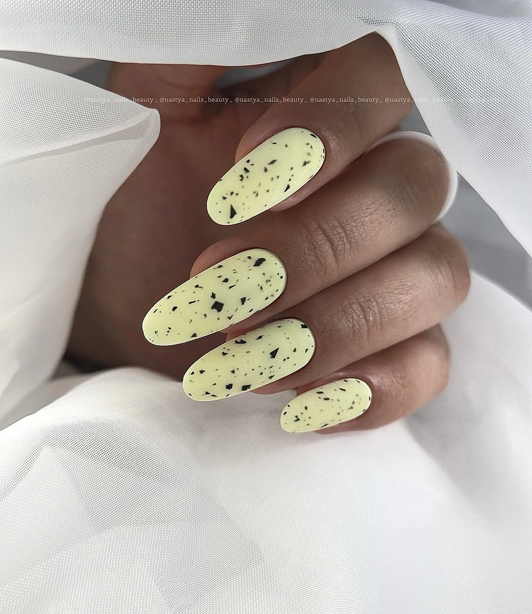 Long almond pale yellow nails with scattered dark speckles