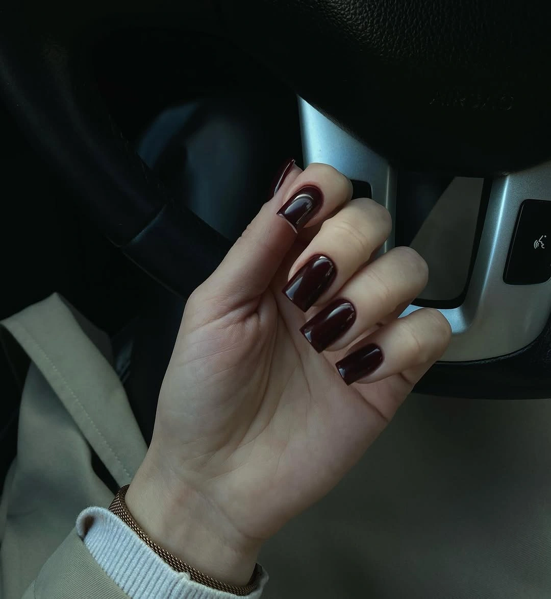 Medium almond nails in dark glossy burgundy under low light