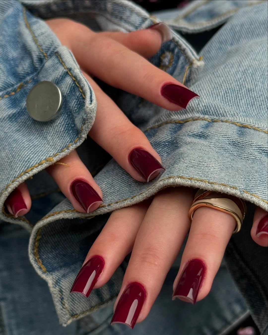 Medium coffin nails in glossy burgundy beside a denim sleeve