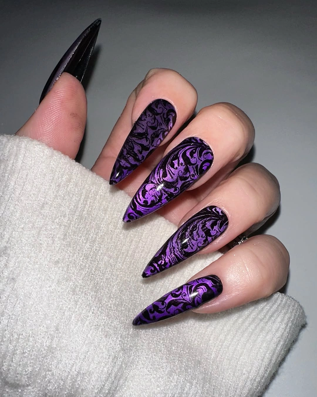 Long purple and black stiletto nails with intricate curling linework