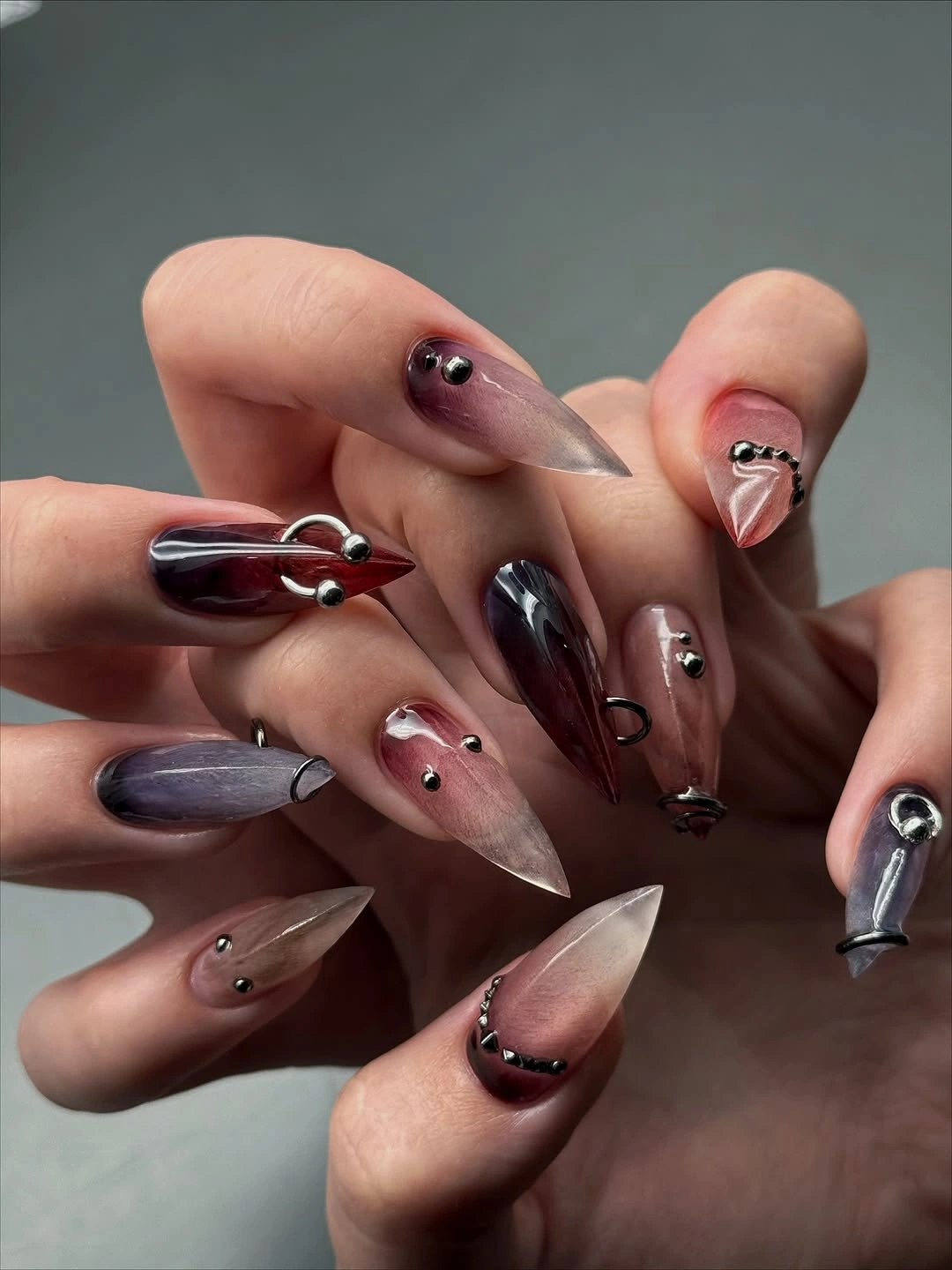 Translucent pointed nails with smoky burgundy curves and small studs