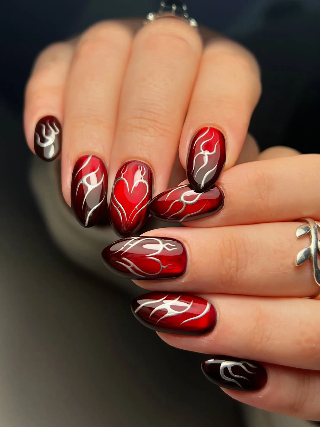 Glossy red and burgundy almond nails with pale flowing line art
