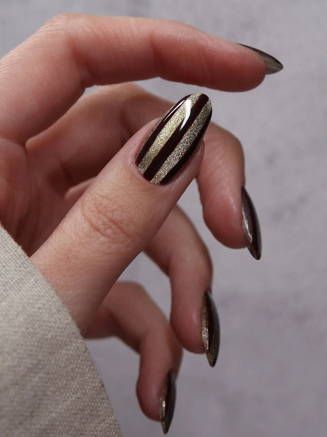 Dark brown pointed nail with two slim metallic gold stripes