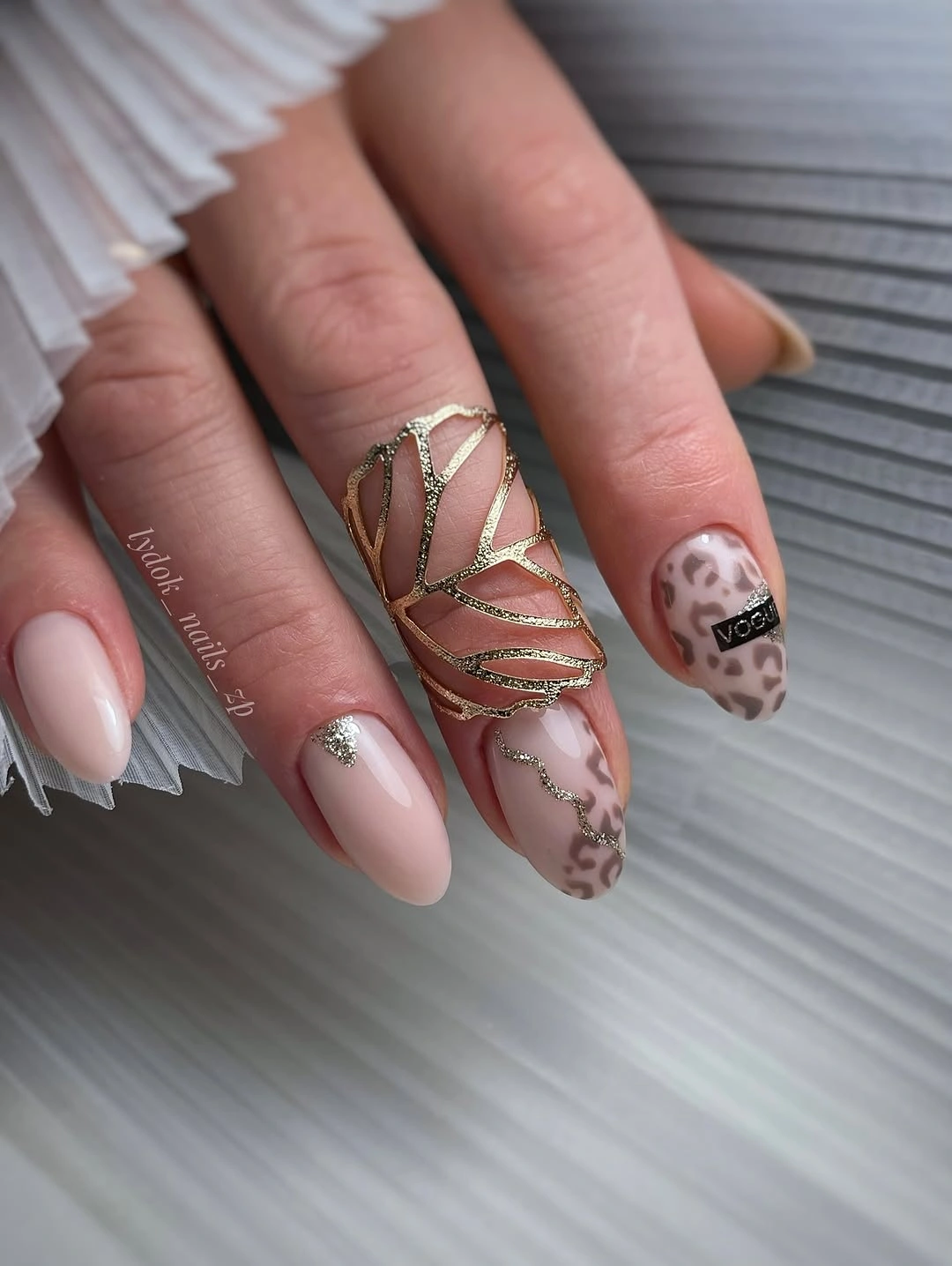 Medium nude almond nails with gold line and patterned accents