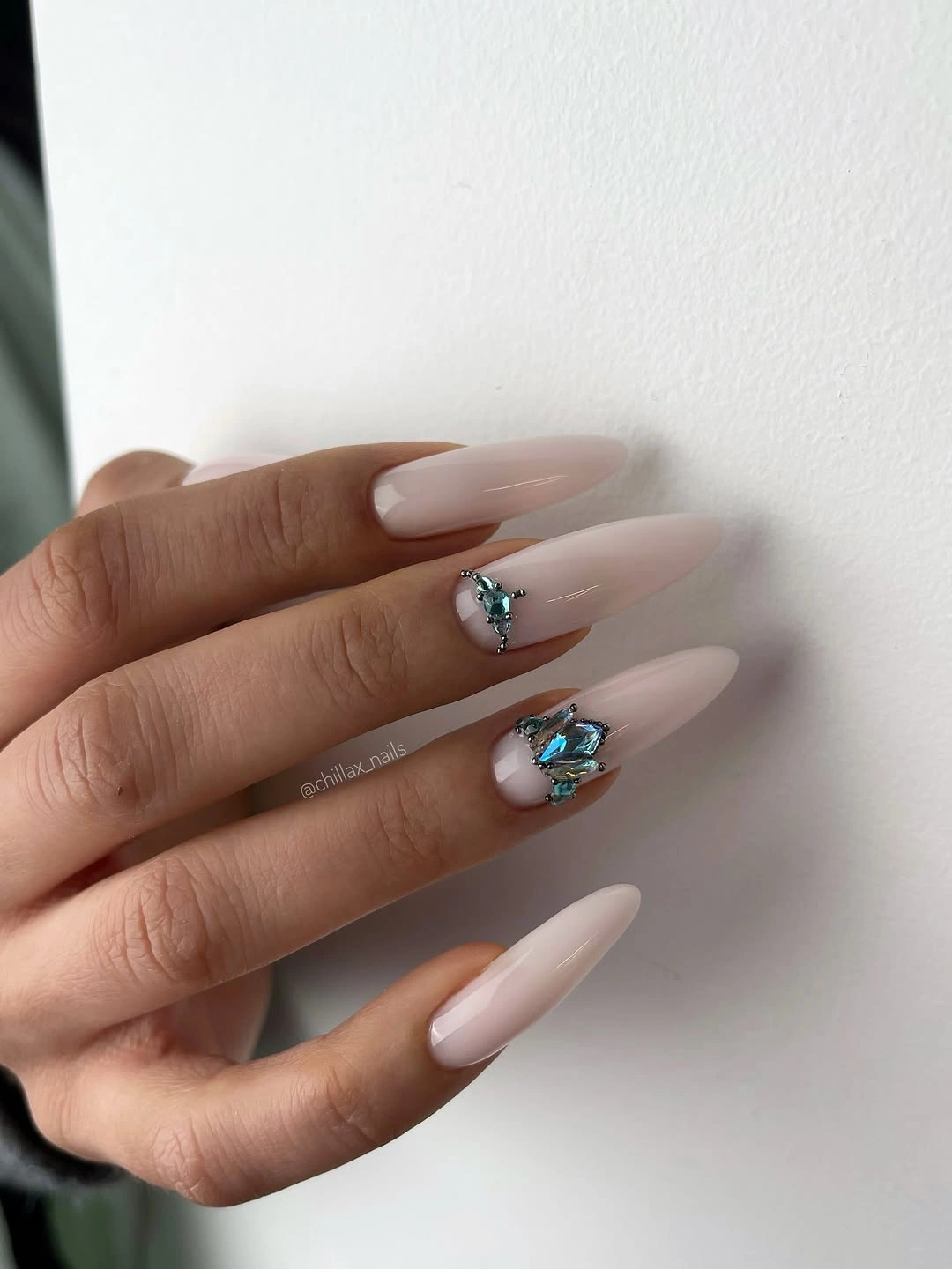 Long pale nude nails with blue floral and gem-like accents