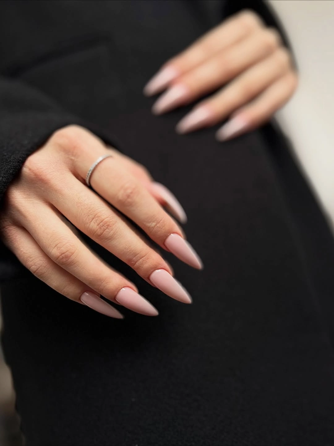 Long glossy pale pink almond nails on a dark background