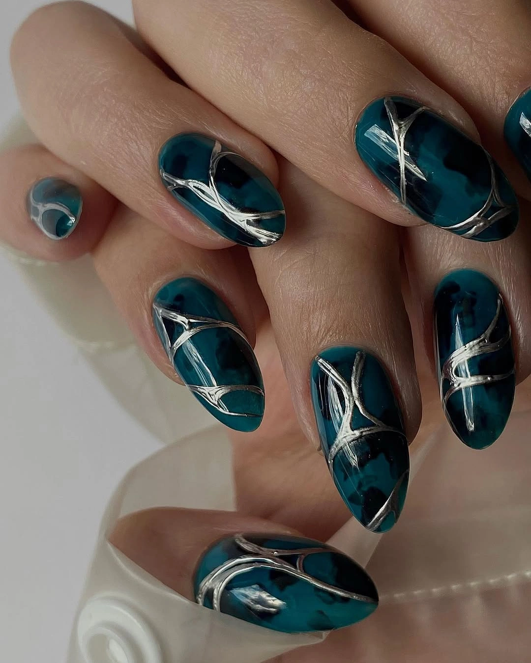 Long glossy teal nails with curved silver abstract linework