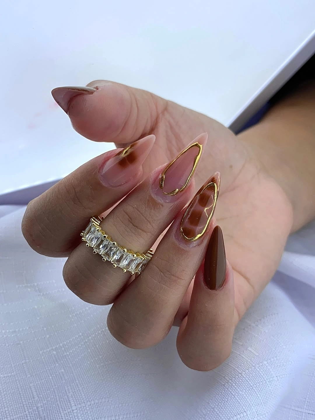 Long almond nude nails with thin gold outlines and burgundy accent