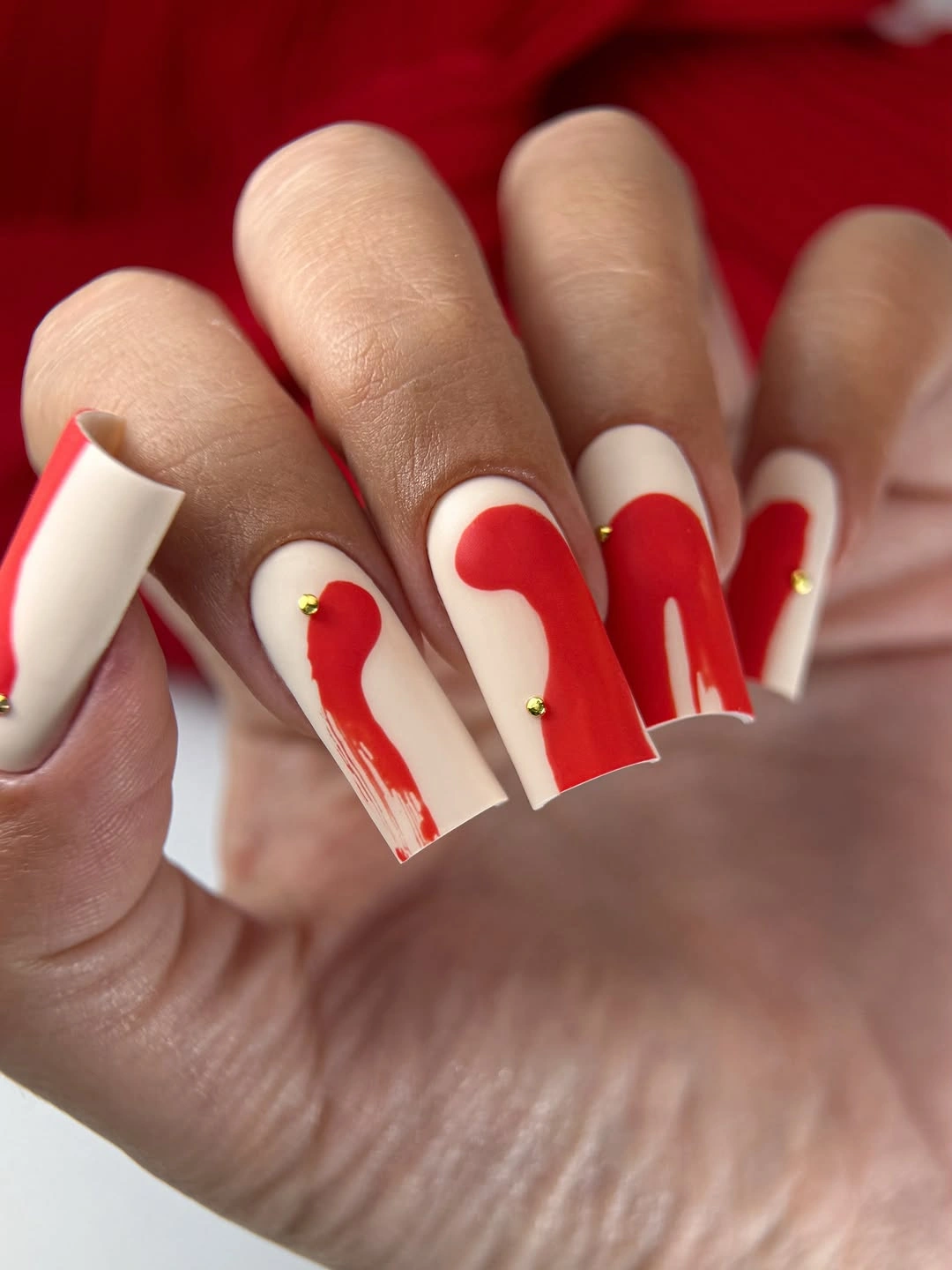 Long white square nails with red abstract swipes and gold dots