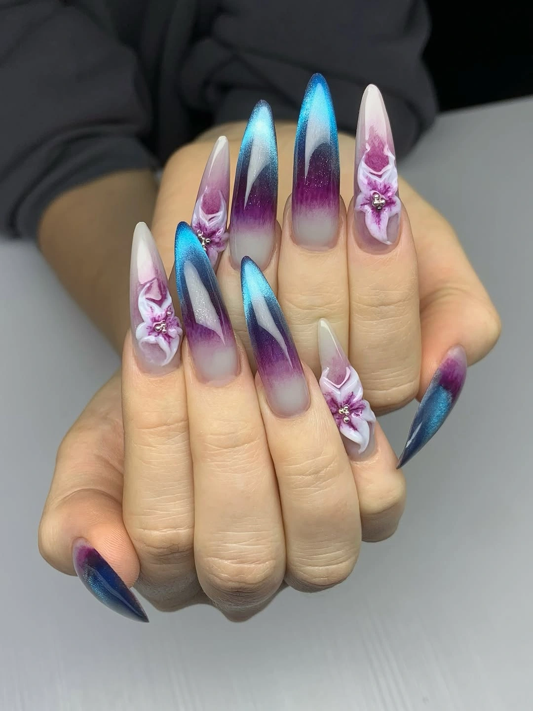 Long pointed nails with blue violet gradient and raised floral accents