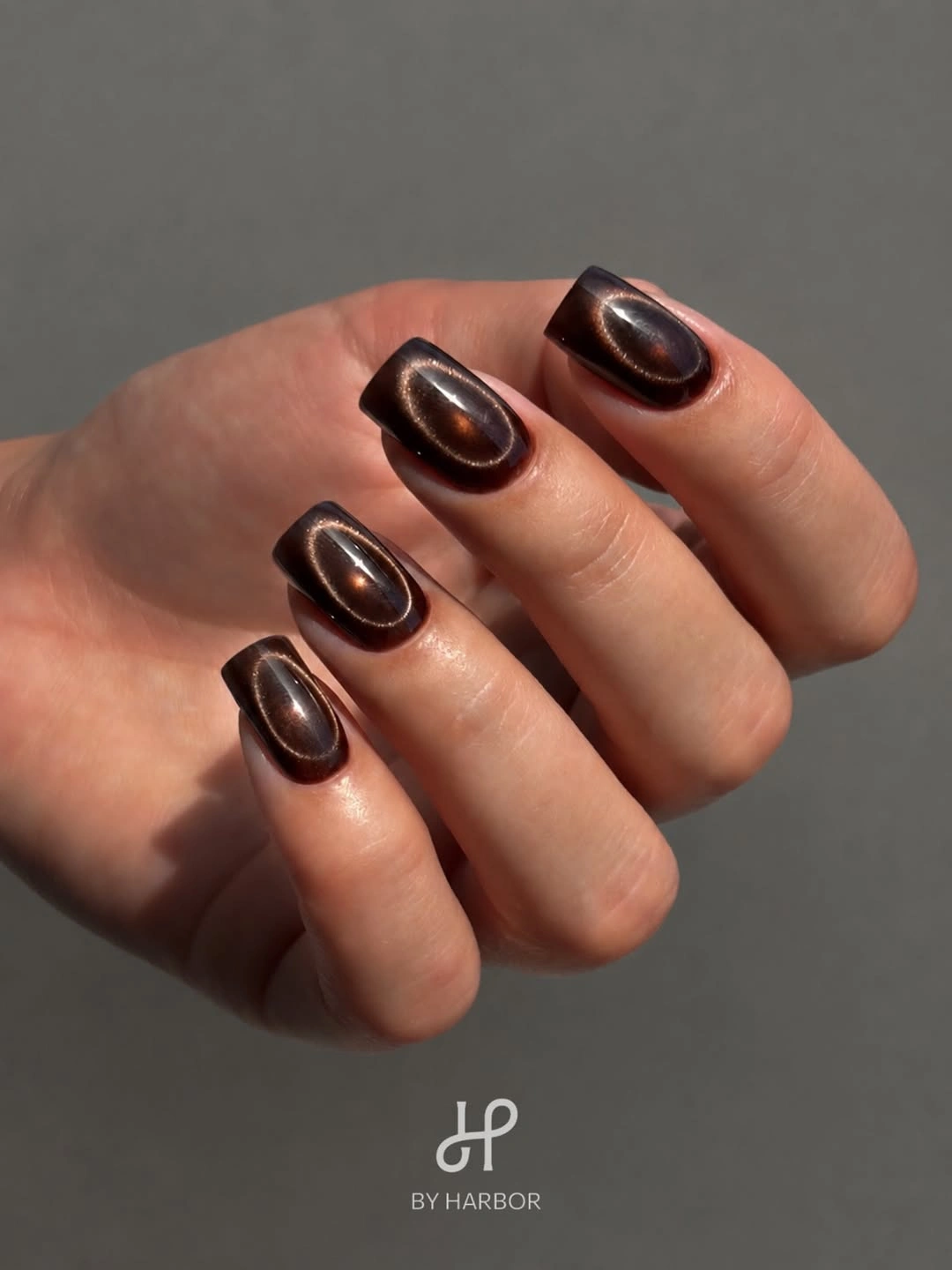 Short rounded brown nails with centered metallic cat eye glow