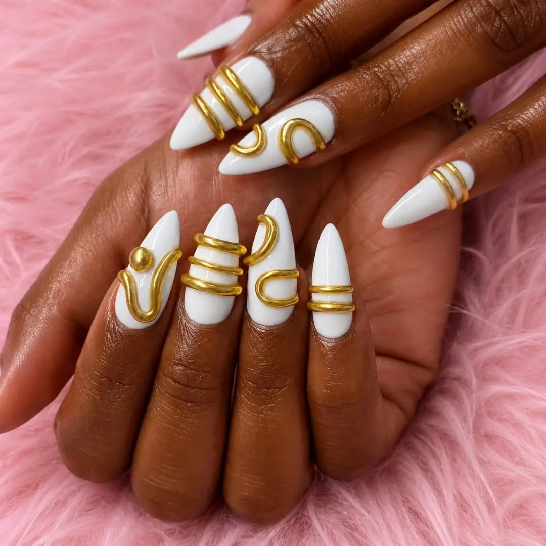 Long white stiletto nails with curved gold line accents