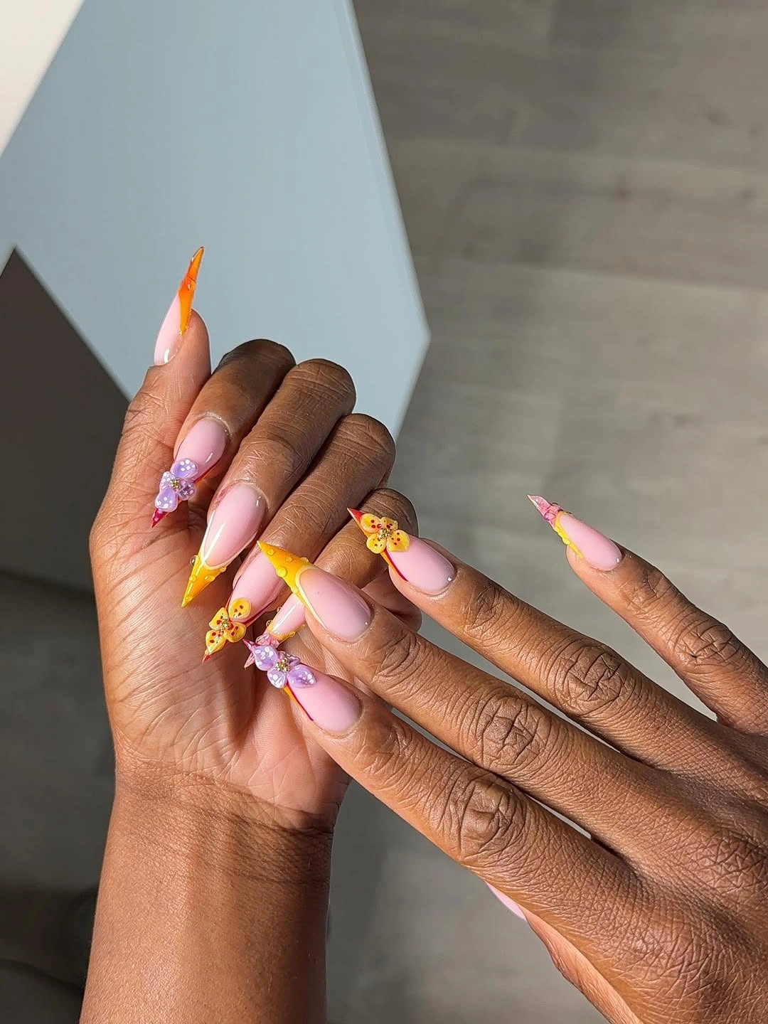 Long pink stiletto nails with colorful tips and purple flowers