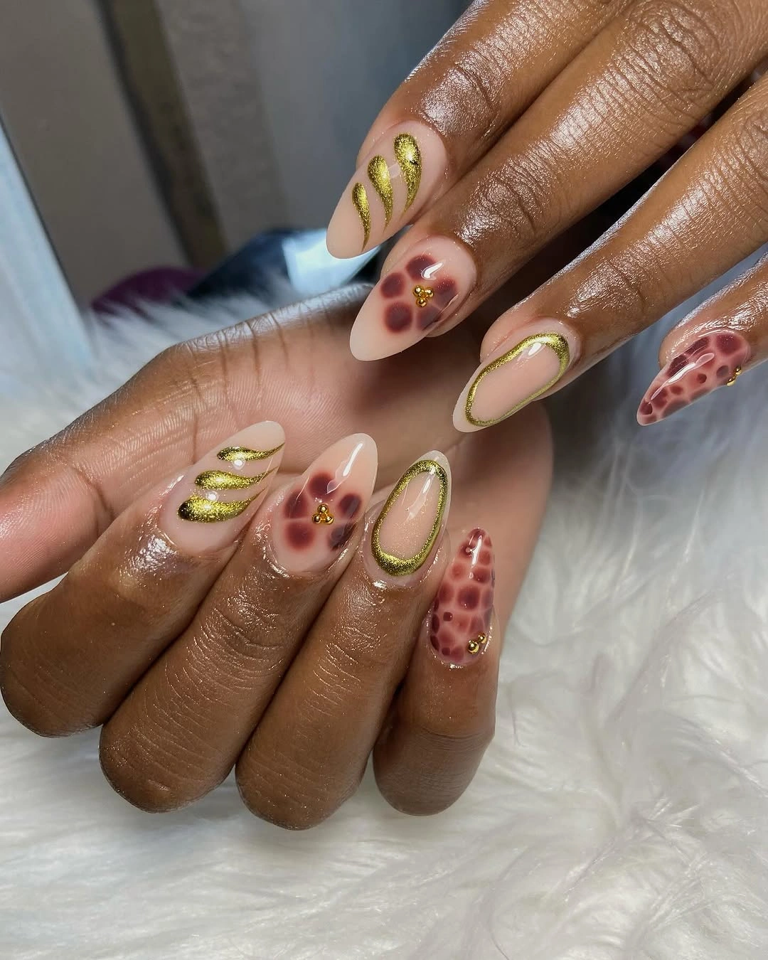 Gold curved almond nails with burgundy spotted accents