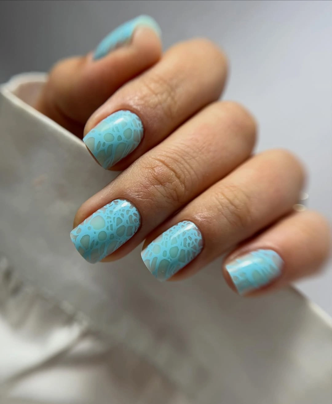 Compact blue nails with a repeated pale textured pattern
