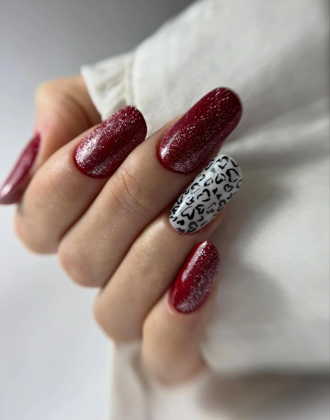 Deep burgundy glitter nails with one black patterned accent