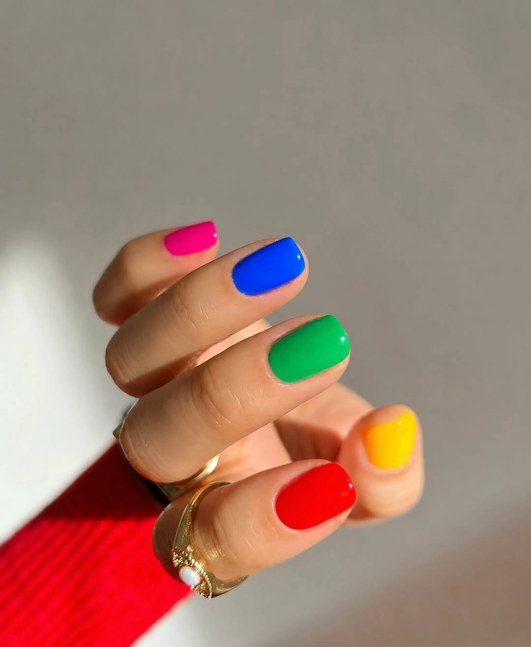 Short rounded nails painted in separate bright rainbow colors