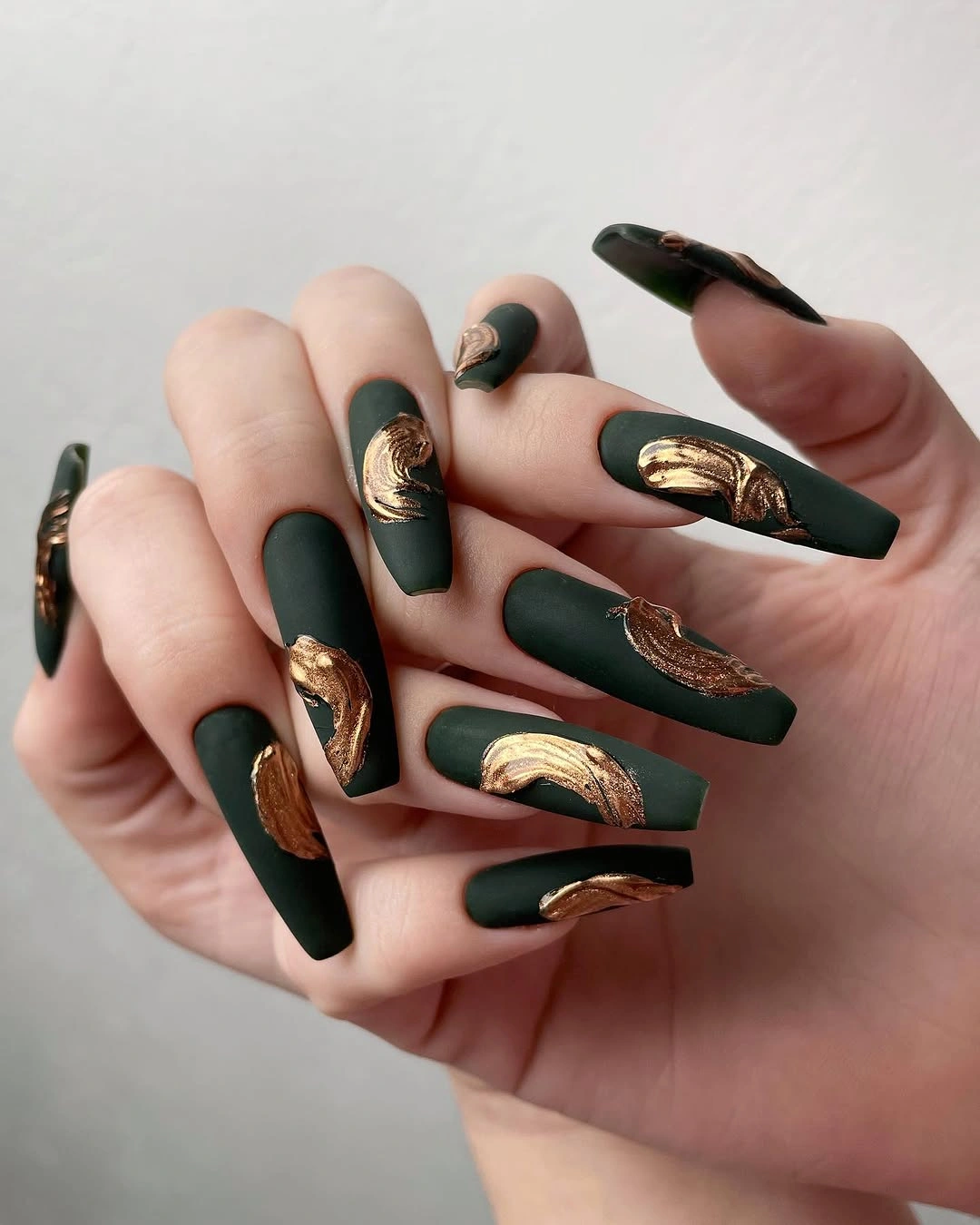long forest green nails with broad gold-looking accent shapes