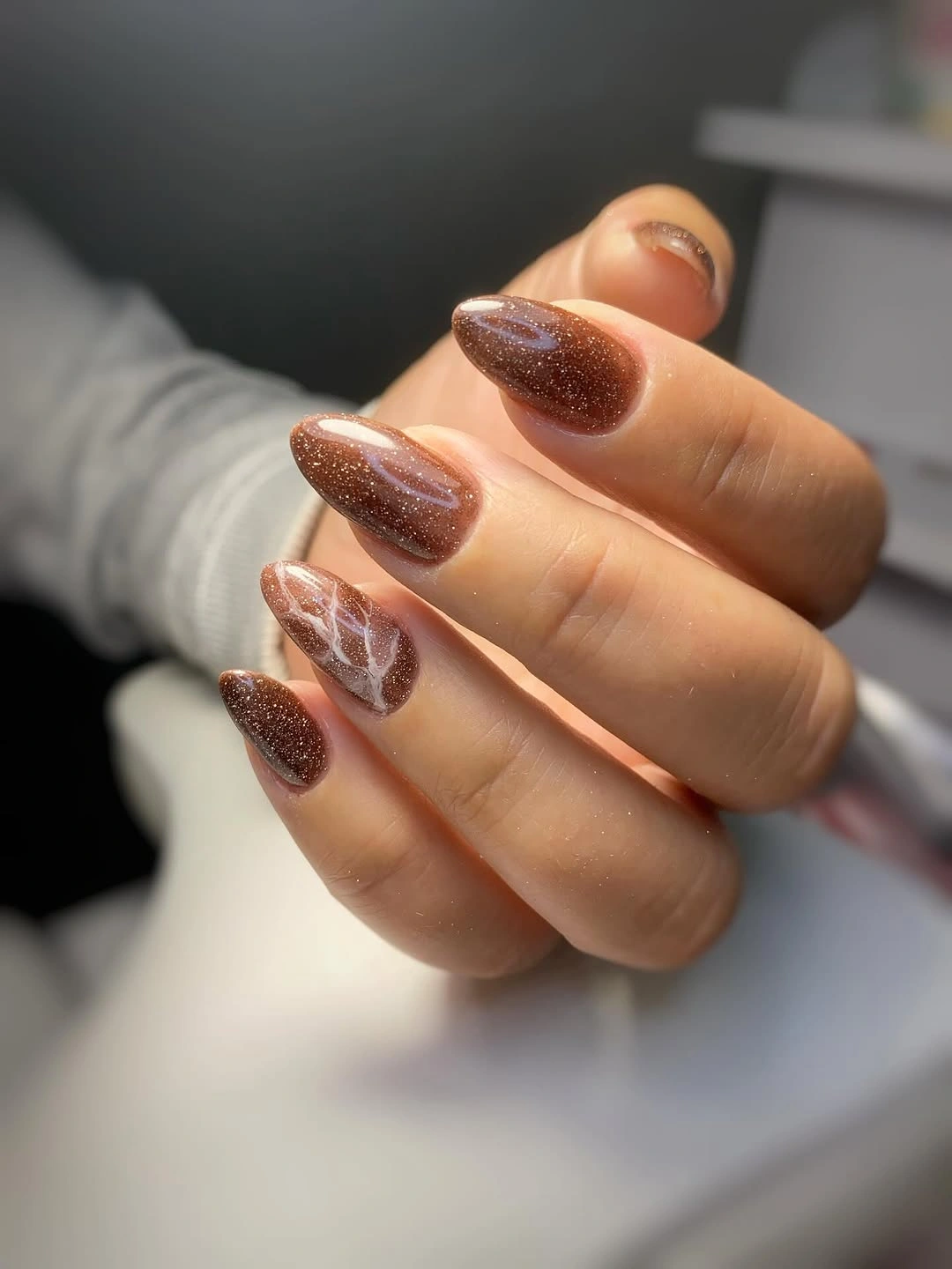 Medium almond nails with brown glitter and one pale marble accent