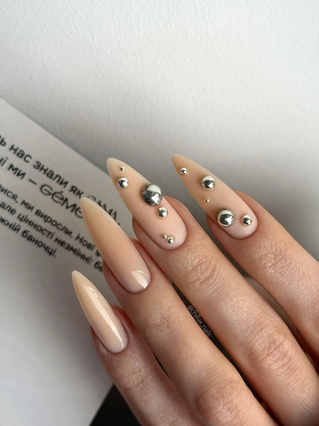 Long nude almond nails with varied silver stud placement
