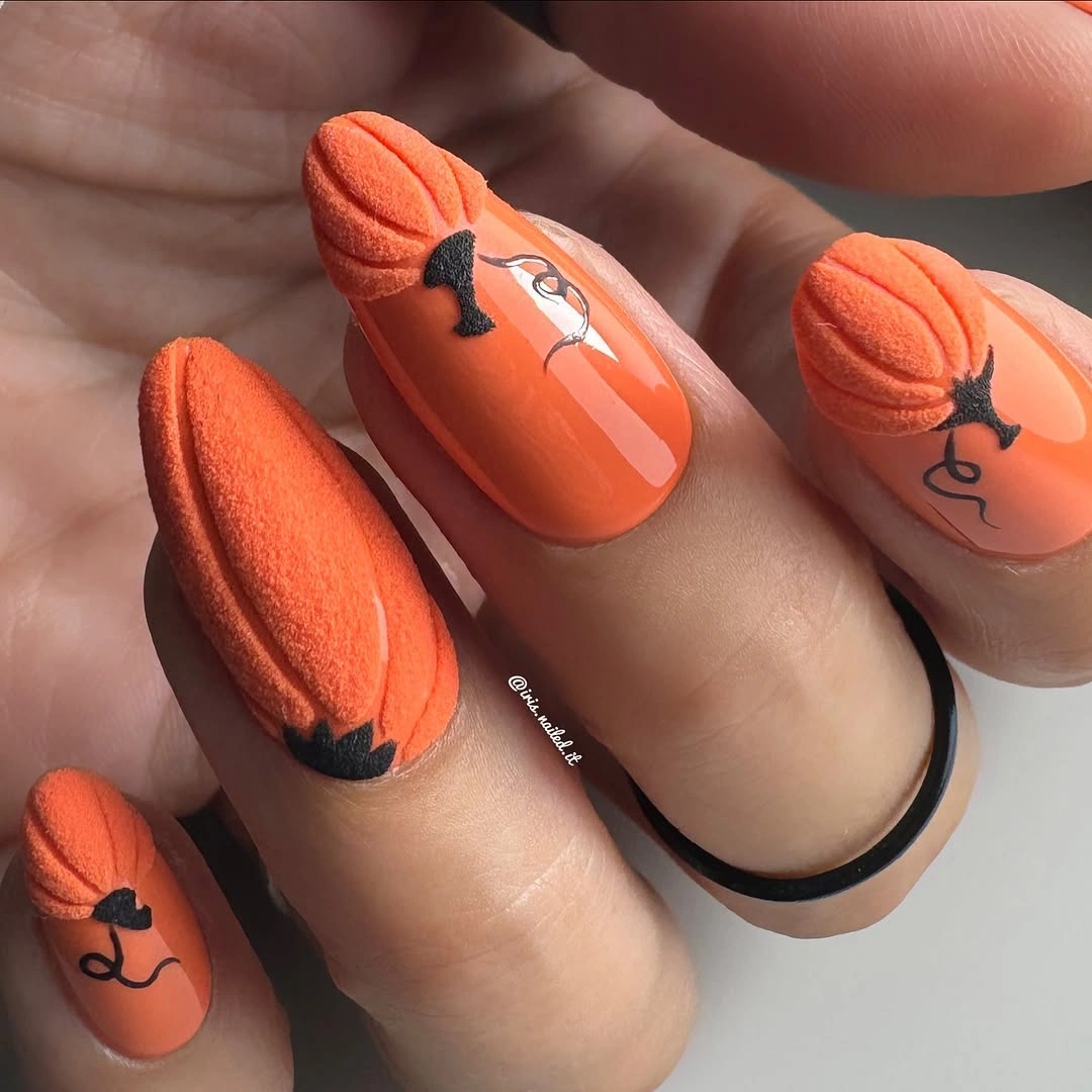 Long orange pumpkin-inspired fall nails with raised texture and black jack-o-lantern details