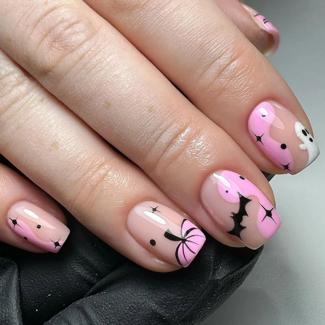Short oval pink nails with playful black and pumpkin-inspired cartoon motifs