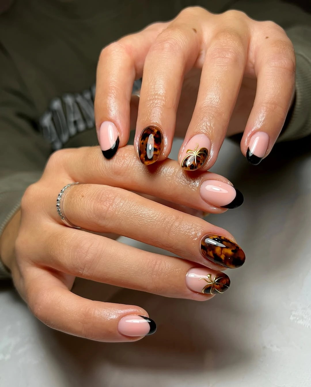 Long nude pink almond nails with black French tips, tortoiseshell, and gold accents