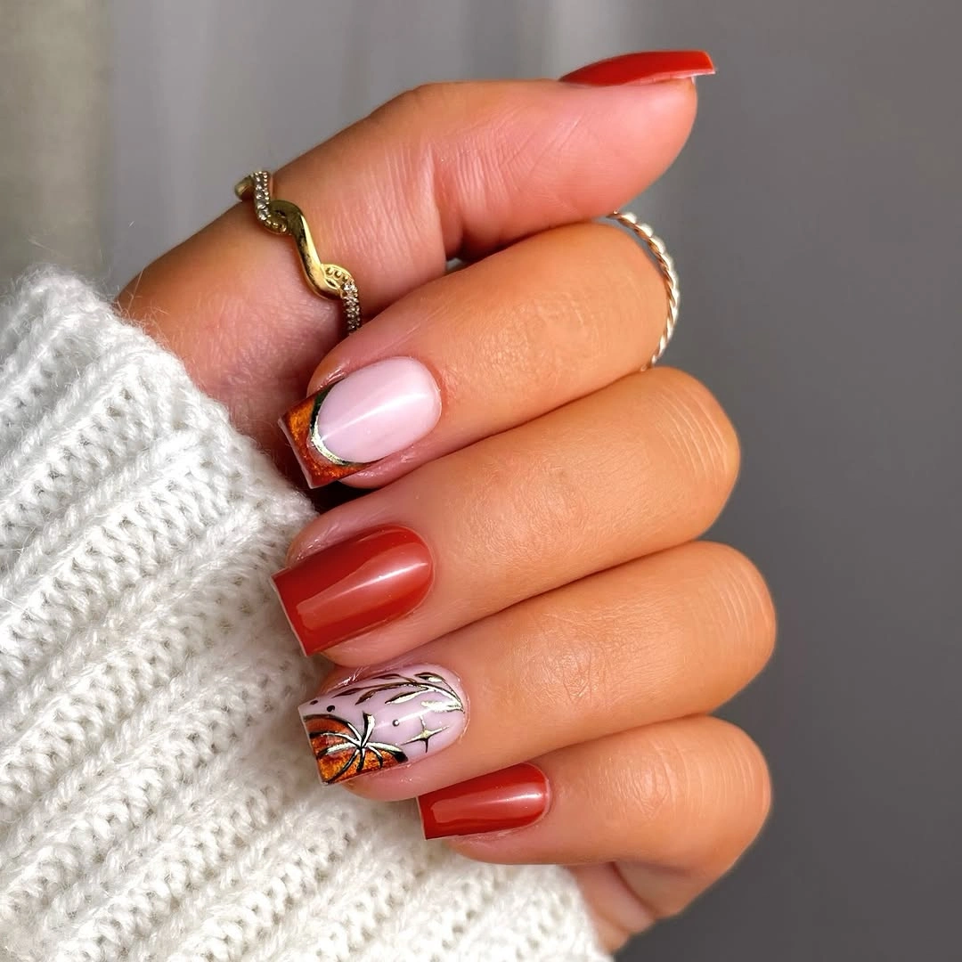 Nude pink fall nails with red and orange solid accents and one black pumpkin detail