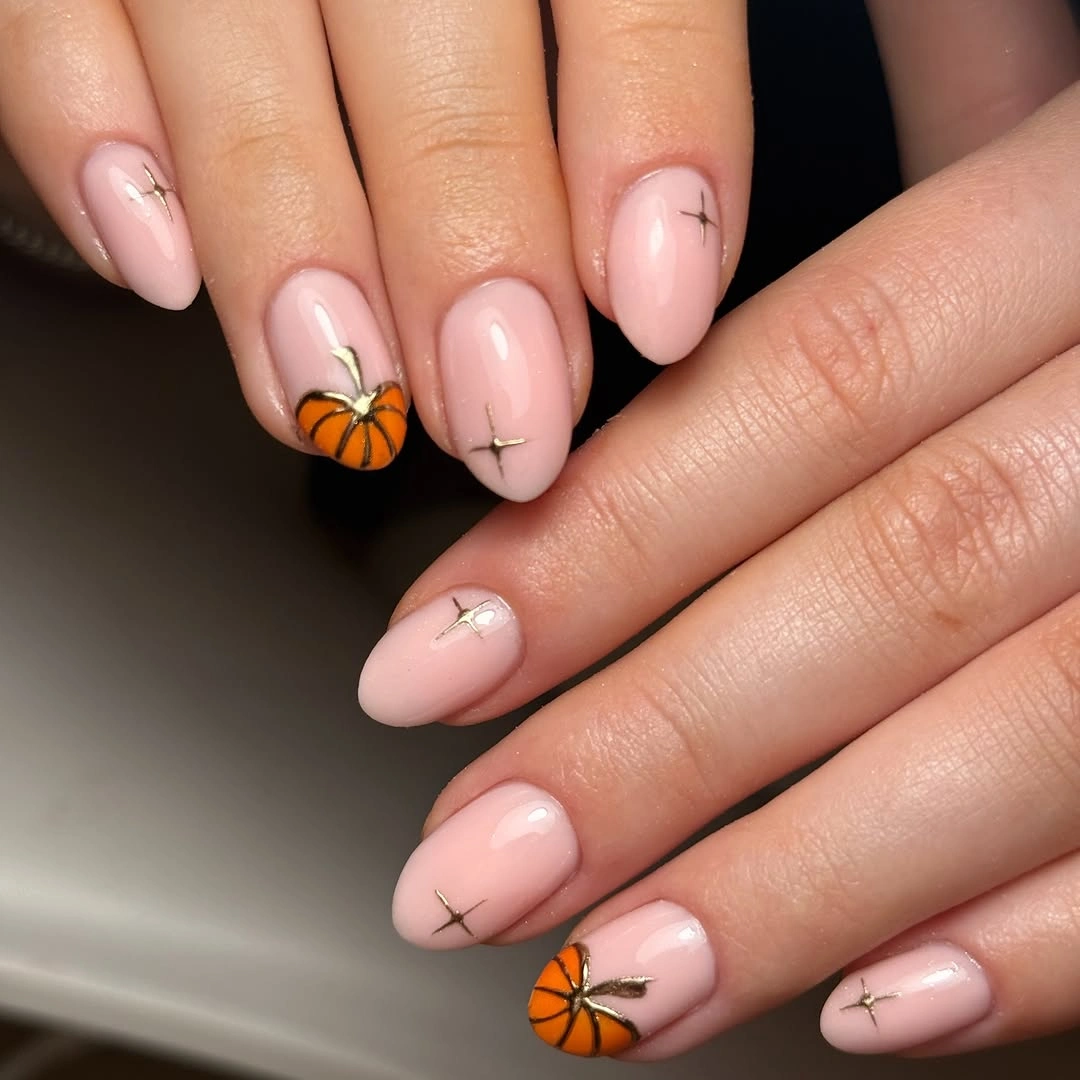Pale pink almond fall nails with a tiny orange pumpkin and delicate gold details