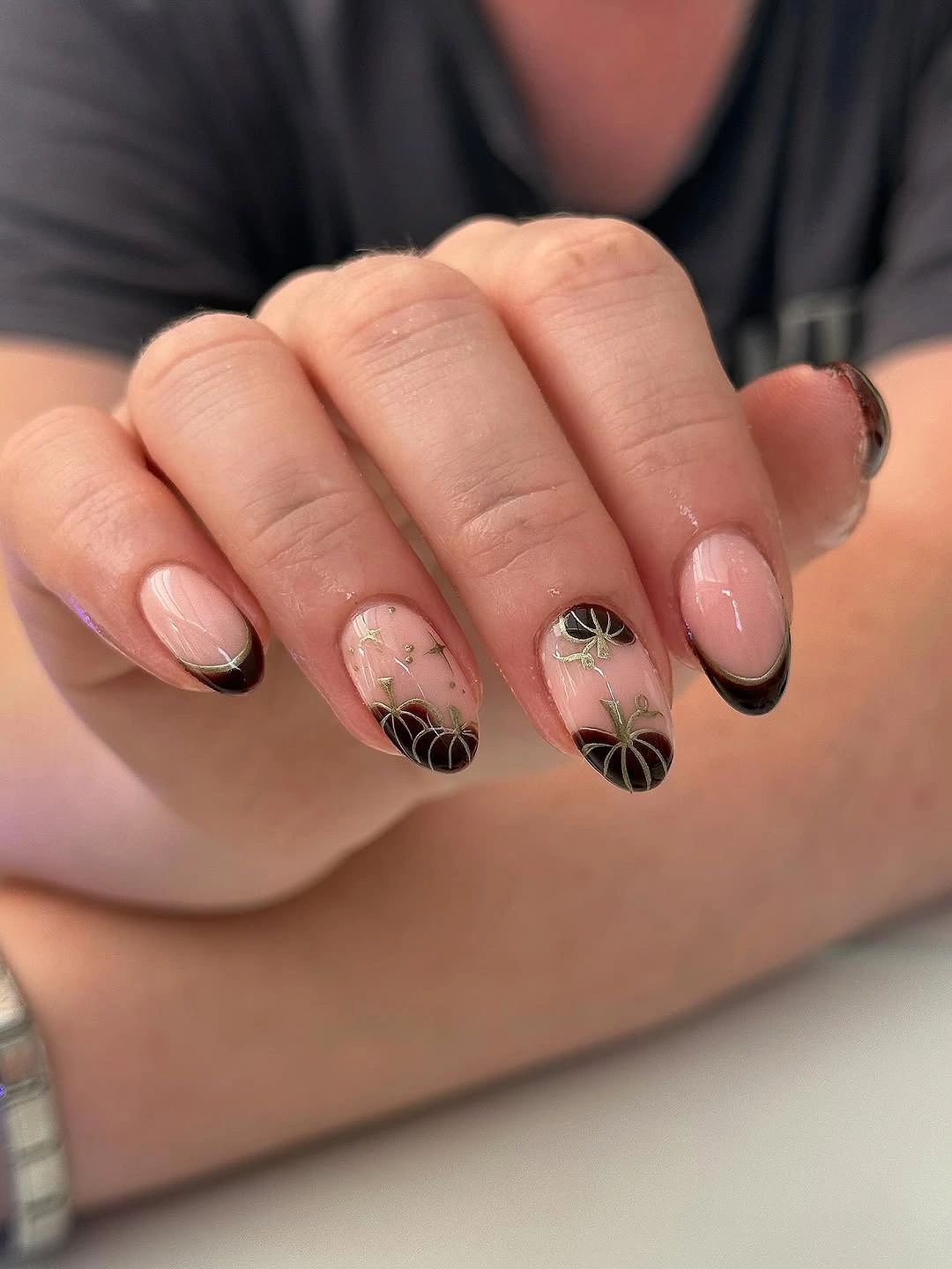 Pale pink fall nails with thin black tips, orange pumpkins, and black botanical accents