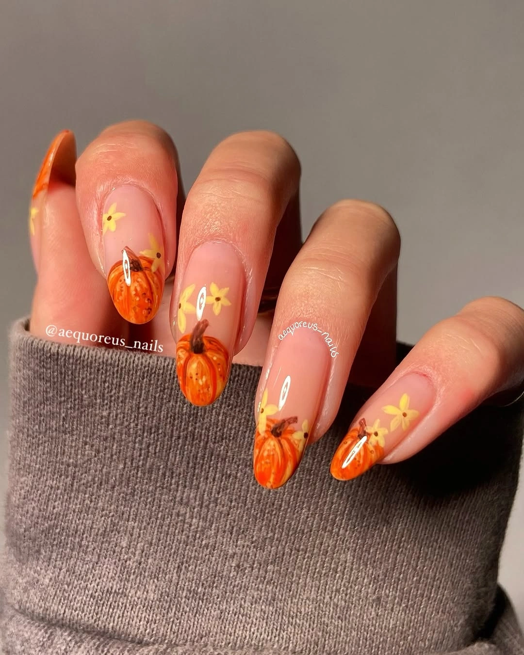 Long orange and pink fall nails covered with pumpkin motifs and yellow star-like details