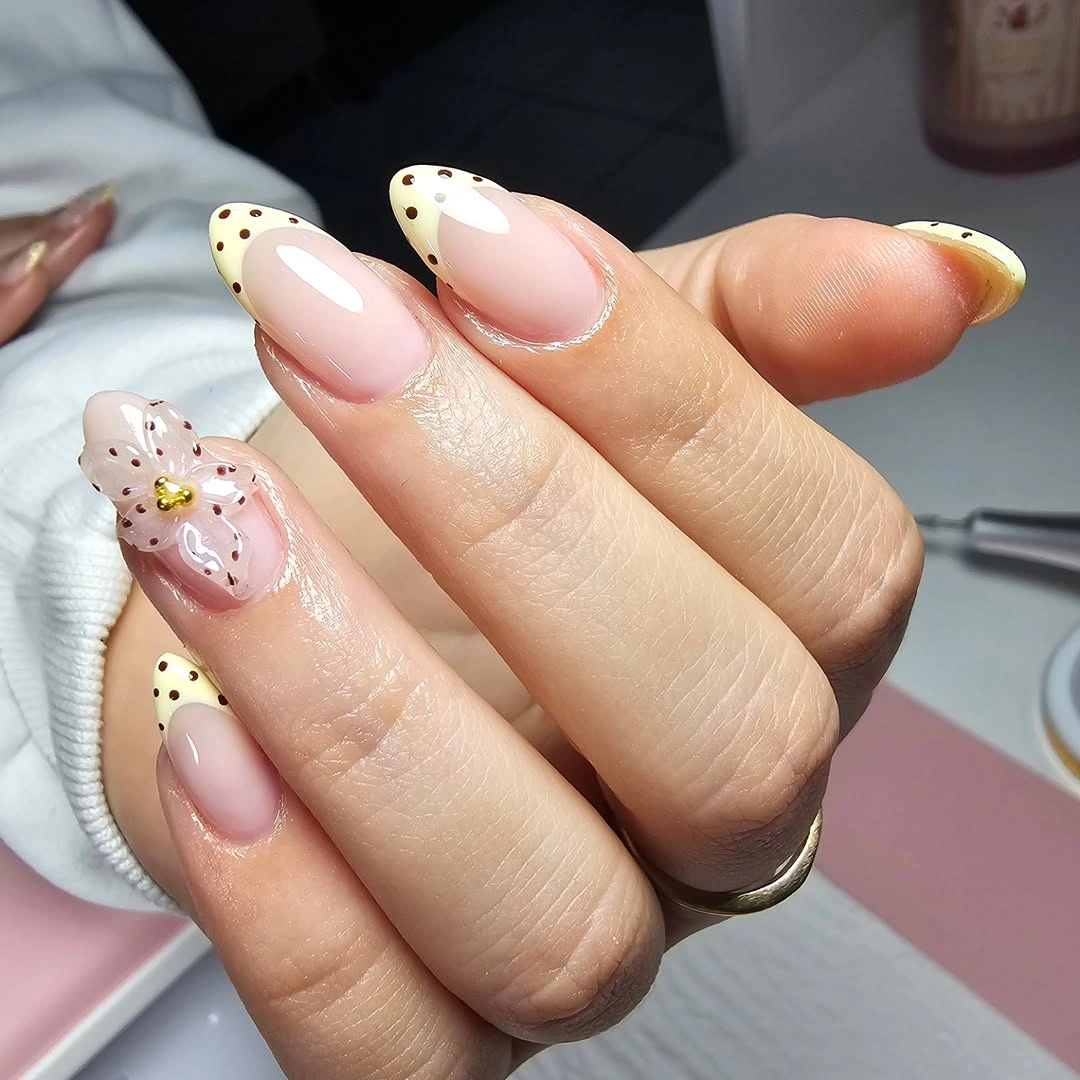 Milky almond nails with black dotted French edges and gold accents