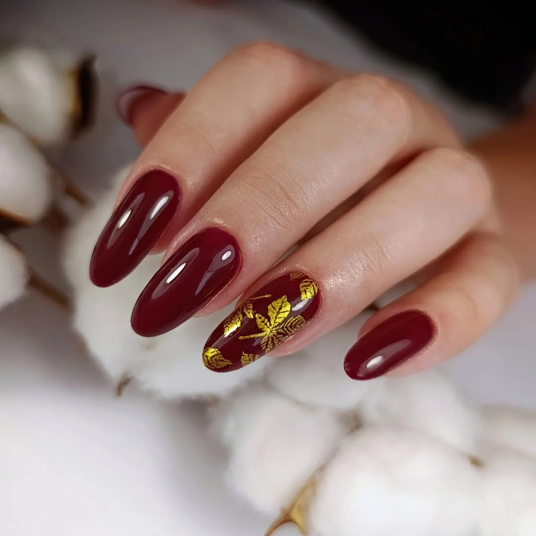 Short burgundy almond nails with one delicate gold botanical accent
