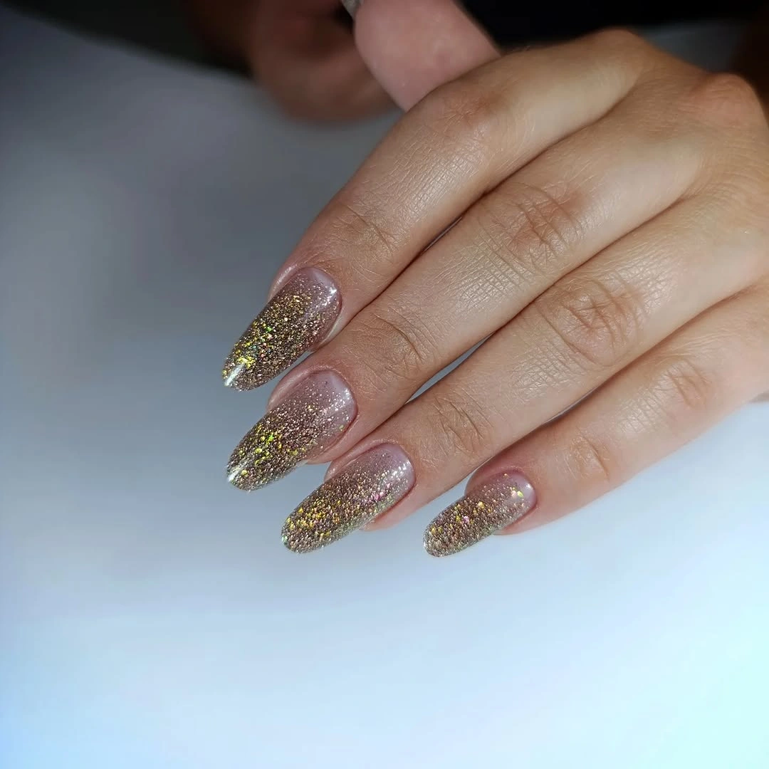 Short almond nails covered in dense champagne gold glitter