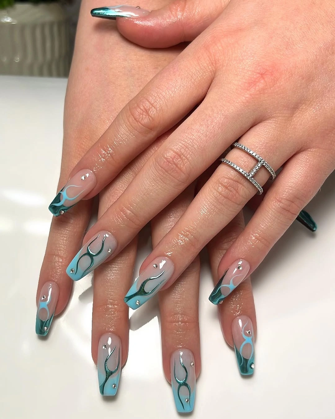 Long tapered coffin nails with teal outlined curves over a taupe base