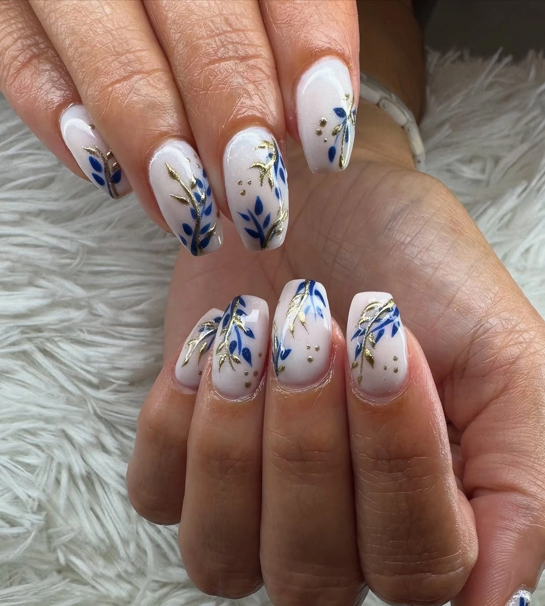Medium almond white nails with blue botanical strokes and tiny accents