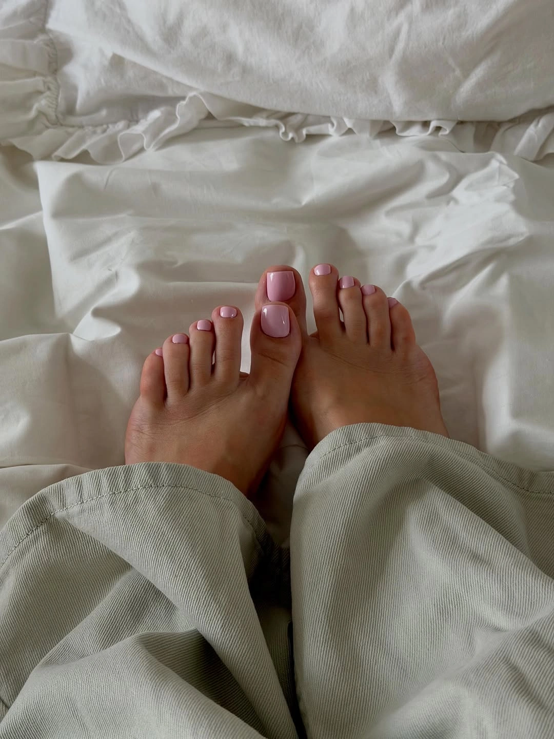 Short pale pink toenails against soft white bedding