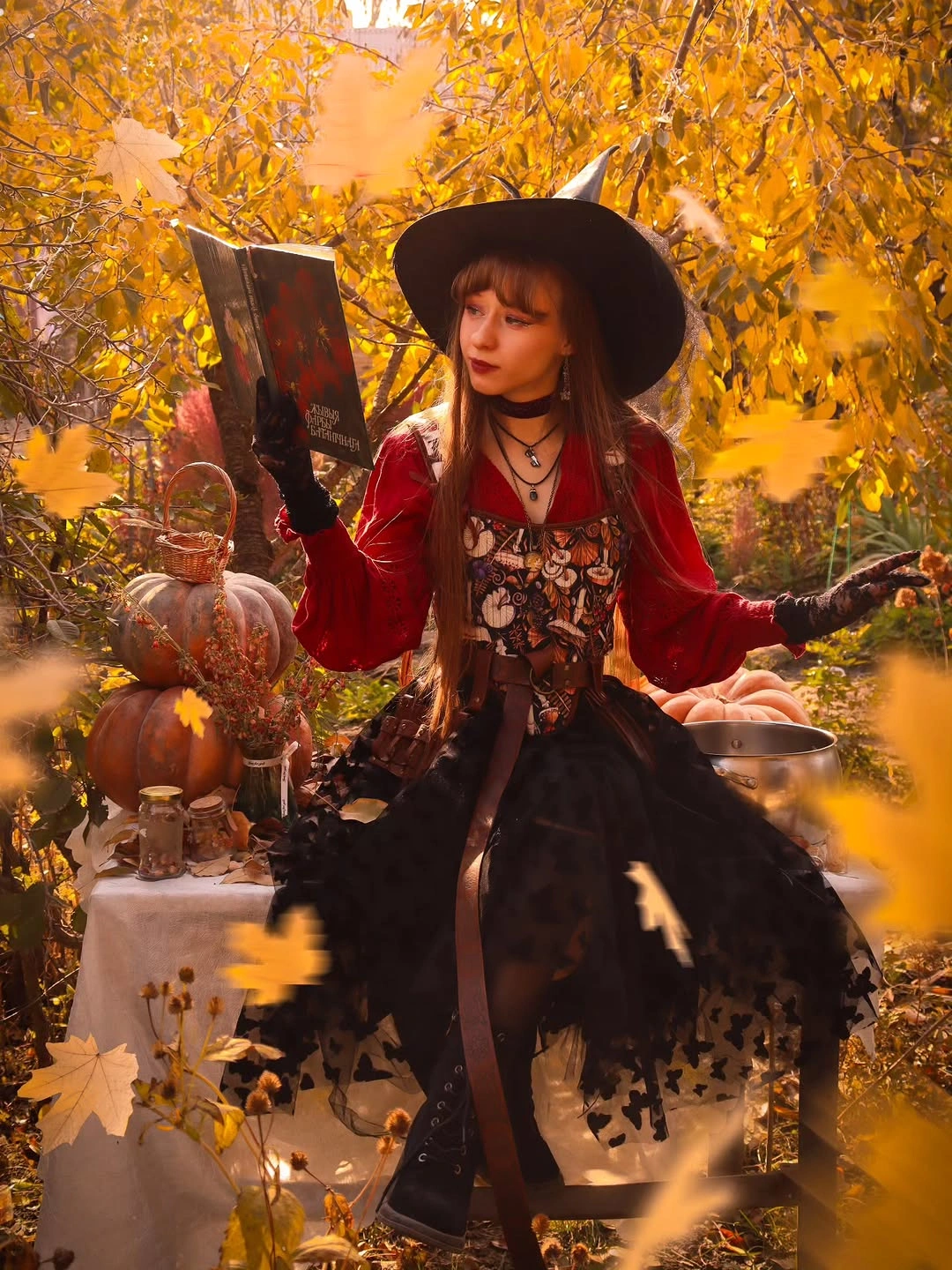 Girl in witch hat red cardigan patterned skirt holding book