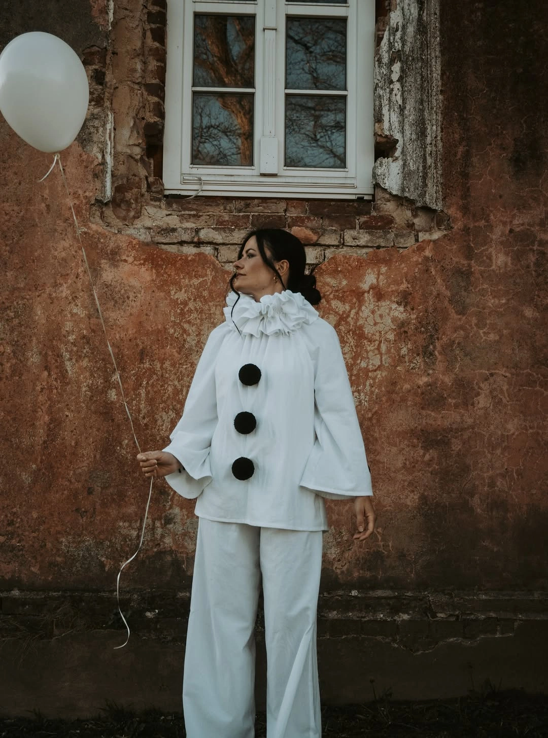 Girl in loose white clown costume with three black pom pom buttons