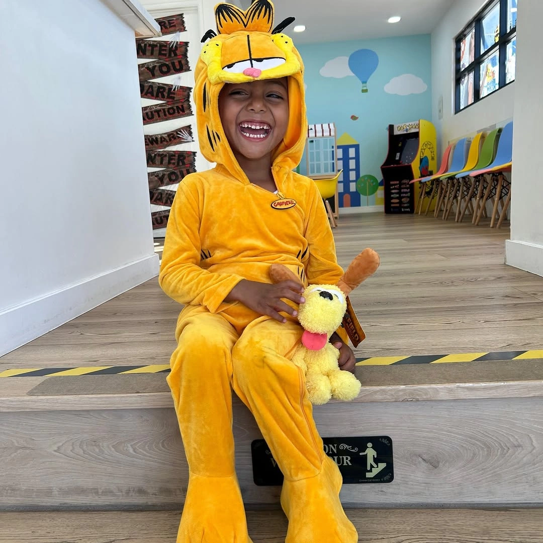 Girl in bright yellow hooded character onesie holding small plush toy