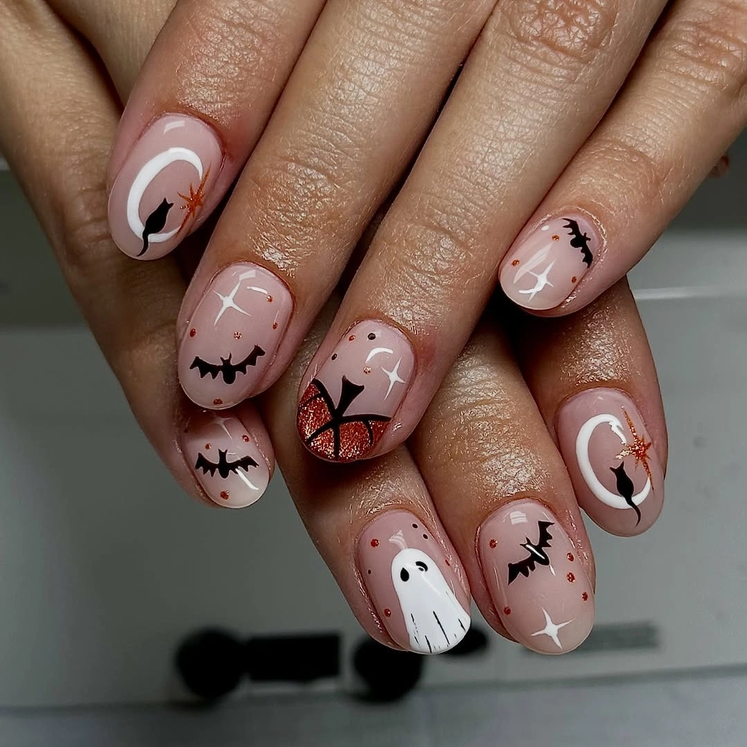 Short to medium pink and nude almond nails with tiny ghosts, bats, and crescent Halloween motifs