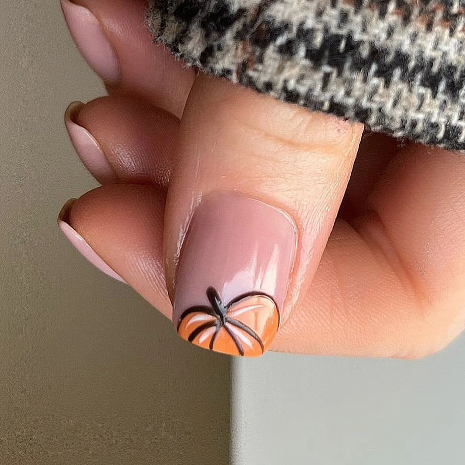 Soft peach nails with dark French edge and detailed pumpkin accent