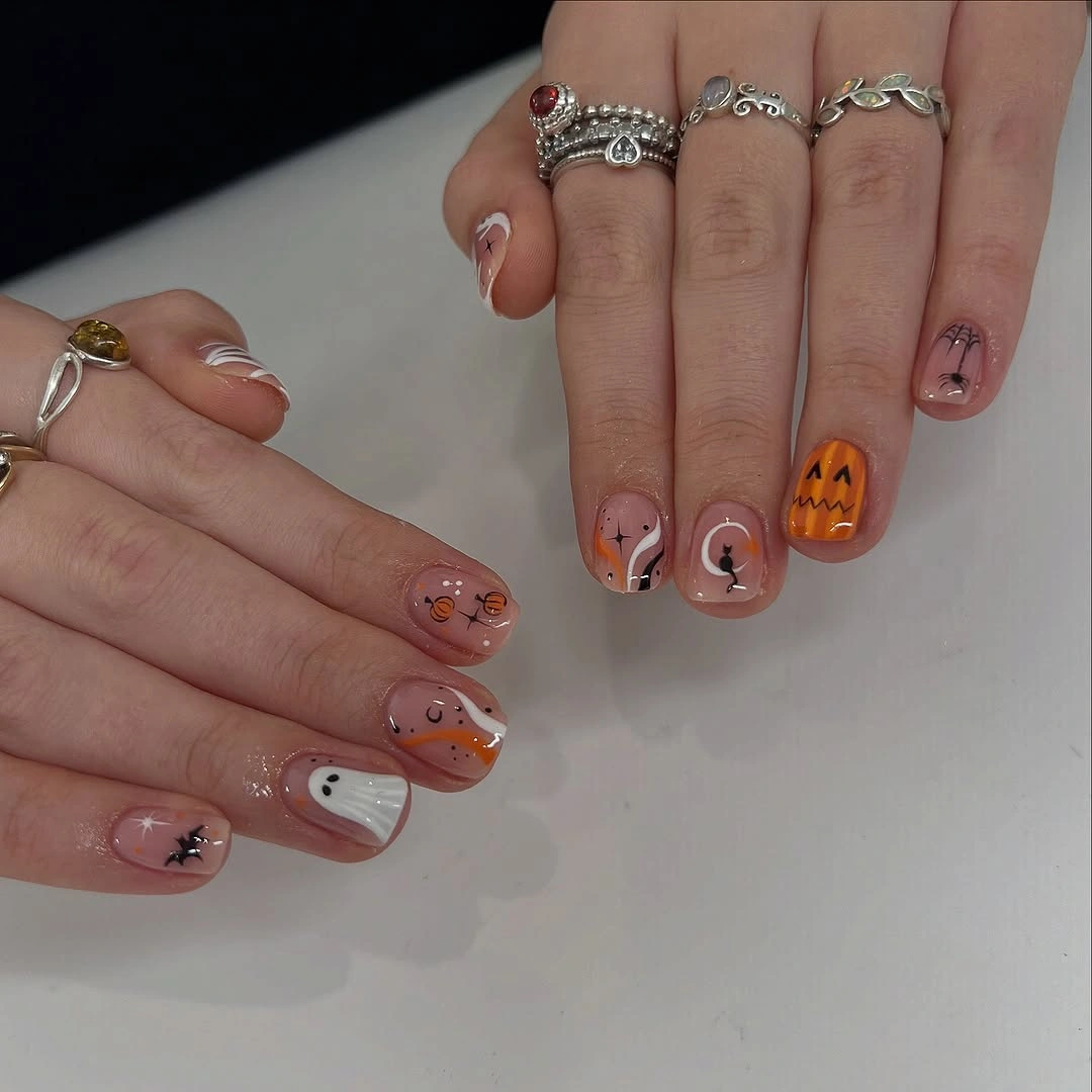 Short nude nails with fine black line art ghosts and pumpkin details