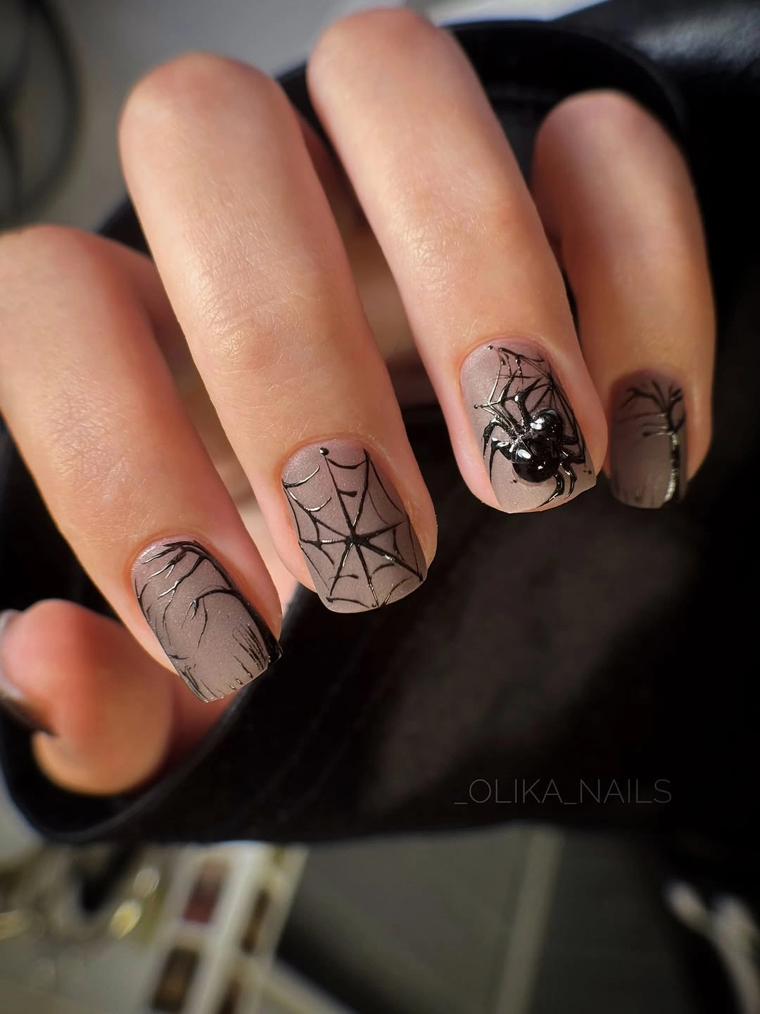 Short to medium nude pink Halloween nails with black spiderweb lines and a spider